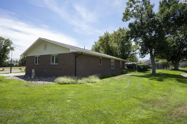 Brick ranch home with a large grassy yard and mature trees.