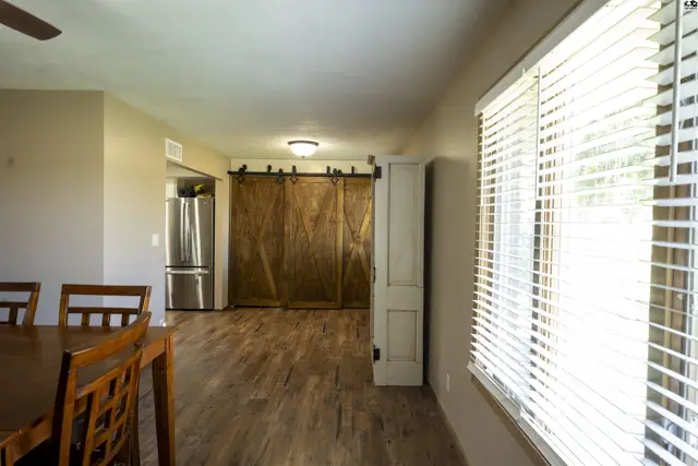 Wood-look flooring extends through this open living area with a stainless steel refrigerator and sliding barn doors.