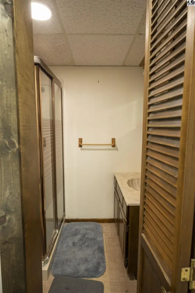 This bathroom features a vanity, a shower stall with glass doors, and a louvered door.