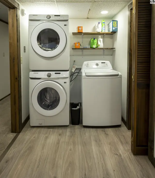 This laundry room features a stacked washer and dryer, a separate washing machine, and shelving.