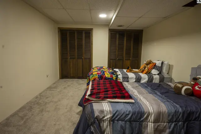 Two beds with striped bedding sit on a carpeted floor in a room with two wooden-paneled closets.