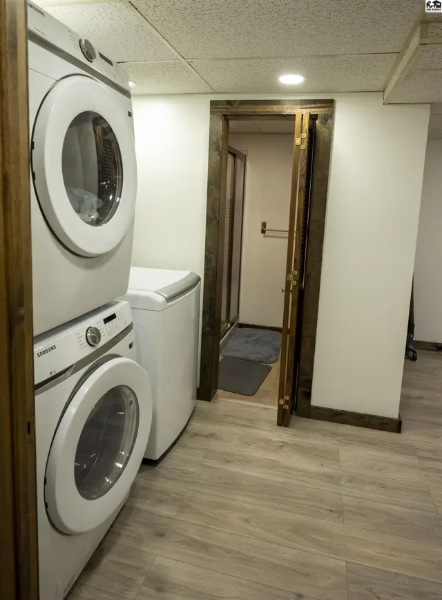 Stacked white washer and dryer beside a white top-load washing machine.
