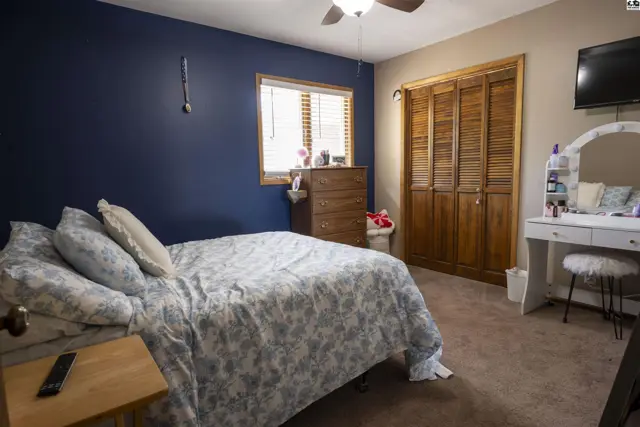 Carpeted bedroom with a queen-size bed, dresser, and wooden closet doors.