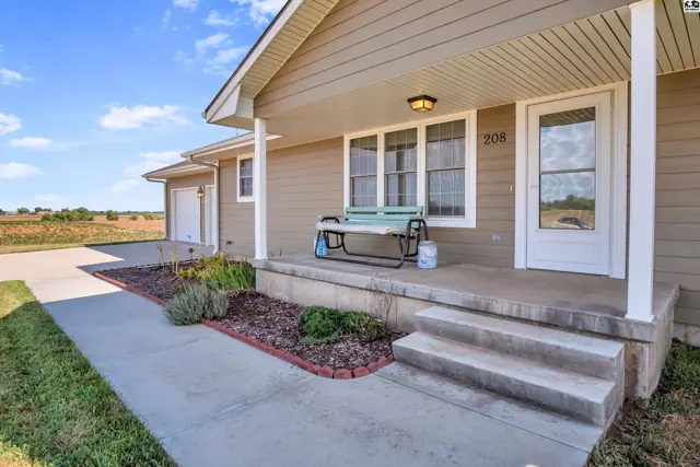 This tan vinyl-sided house features a covered front porch with a bench and a concrete walkway.