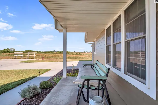 Covered porch with seating overlooks a paved walkway and expansive fields.