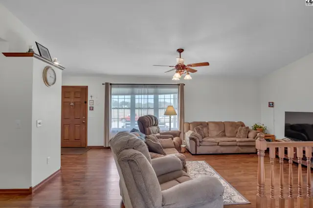 Spacious living room with wood floors, a ceiling fan, and large windows.