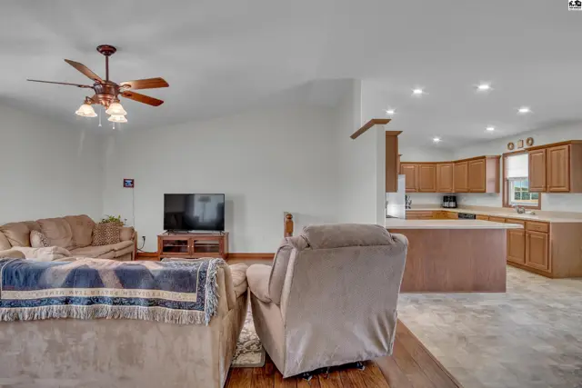 Spacious living area with a ceiling fan opens to a kitchen with wood cabinetry.