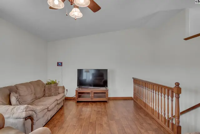 Spacious living room with vaulted ceiling, wood floors, and a wood railing.