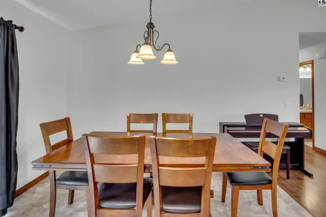 A wood dining table with six chairs is centered in a room with a chandelier.
