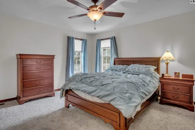 Spacious bedroom with a wooden bed frame, dresser, nightstand, and ceiling fan.