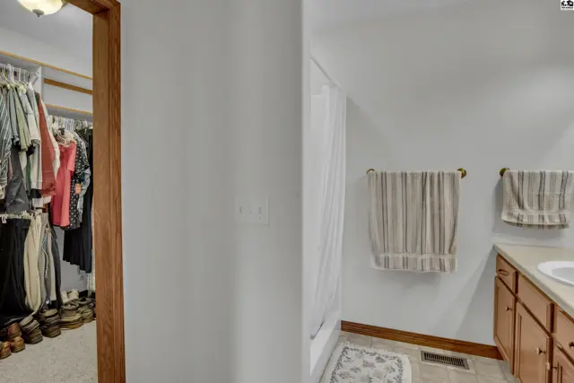 Walk-in closet with clothing and shoes adjacent to a bathroom with a vanity and shower.