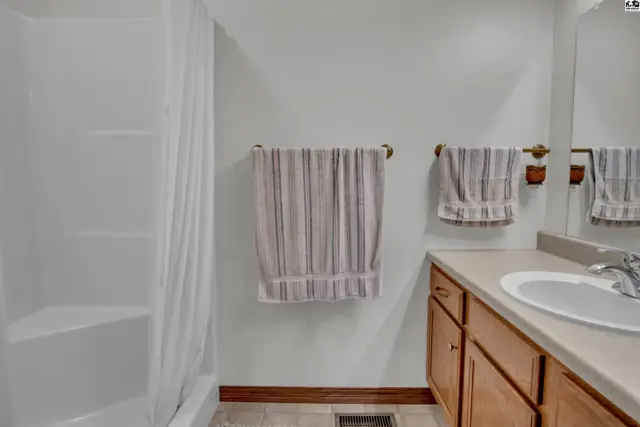 This bathroom features a white tub-shower unit, wood vanity, and light-colored tile flooring.