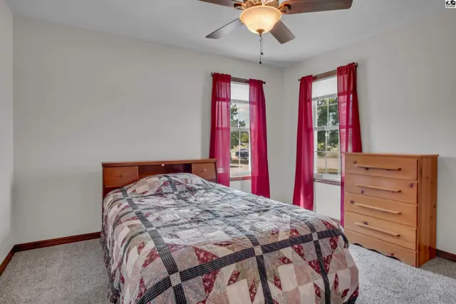 This bedroom features a bed, dresser, ceiling fan, and carpeted floor.