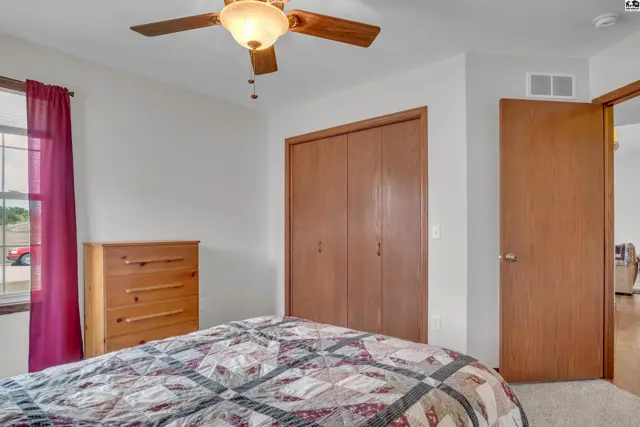 This bedroom features a ceiling fan, a closet with wood doors, and a window with burgundy curtains.