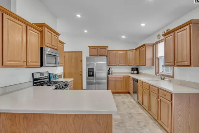 Spacious kitchen features light wood cabinetry, stainless steel appliances, and ample counter space.
