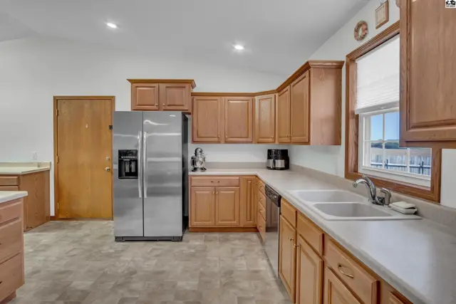 Spacious kitchen features light wood cabinetry, stainless steel appliances, and a double sink.