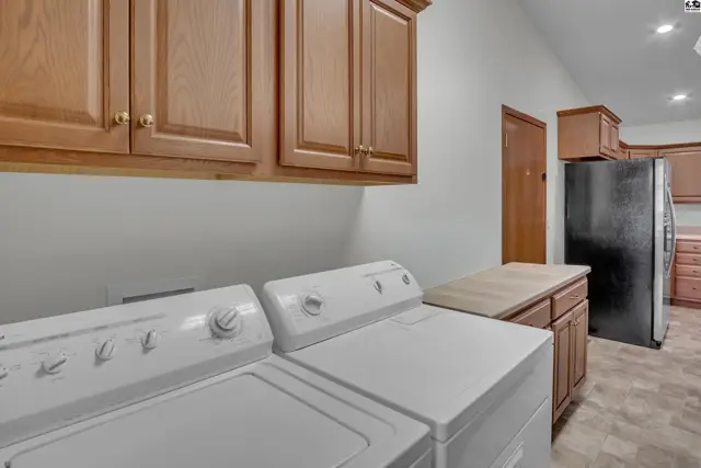 This laundry room features a washer, dryer, wood cabinetry, and a refrigerator.