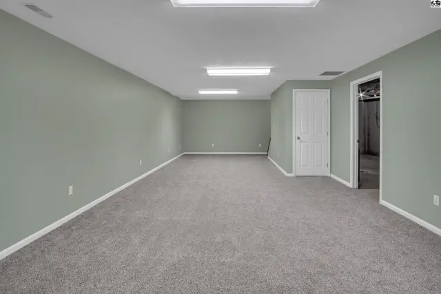 Spacious room with carpeted floor, neutral walls, and overhead lighting.