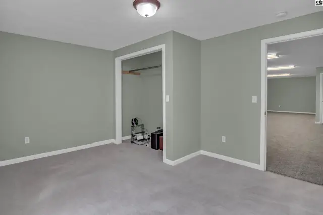 This room features light grey walls, grey carpet, and a closet with a hanging rod.