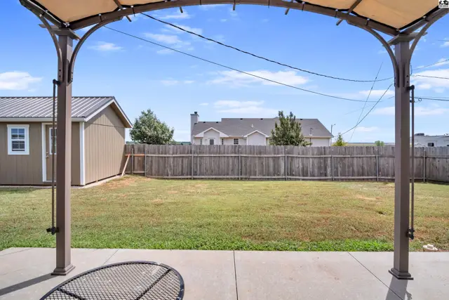 A tan shed and a wooden fence enclose a grassy backyard with a concrete patio.