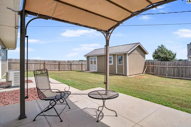 Concrete patio with a metal table and chair is shaded by a tan awning.