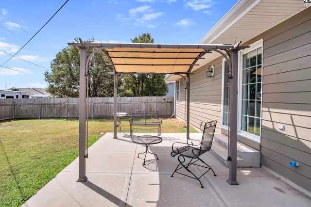 A metal pergola with a tan fabric canopy covers a concrete patio with outdoor seating.