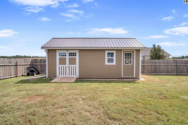 Brown shed with a metal roof and two doors sits in a grassy yard.