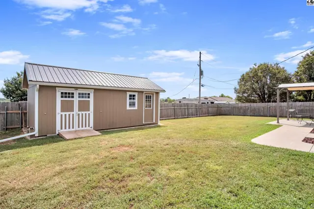 A brown shed with a metal roof sits in a grassy yard with a wooden fence.