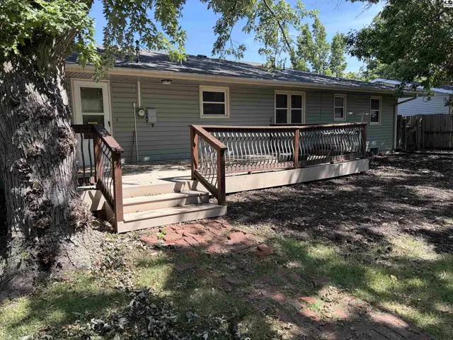 Spacious wooden deck with railing and stairs extends from the rear of the light-colored siding house.