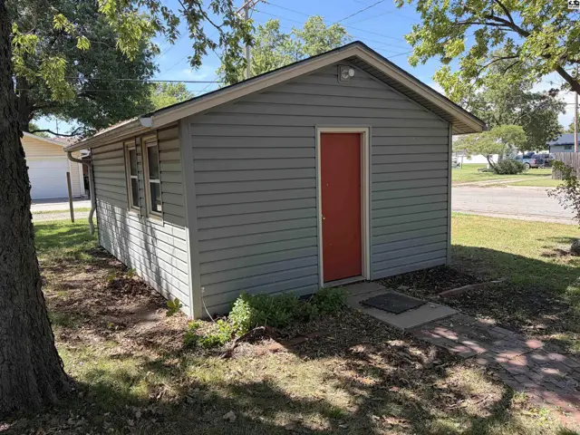 Gray vinyl siding covers this detached structure with a red door and two windows.