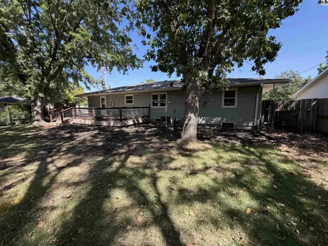 A large wooden deck extends from the rear of this light green, single-story home.