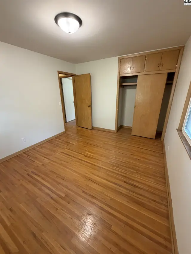 This bedroom features hardwood floors and a built-in closet with wooden doors.