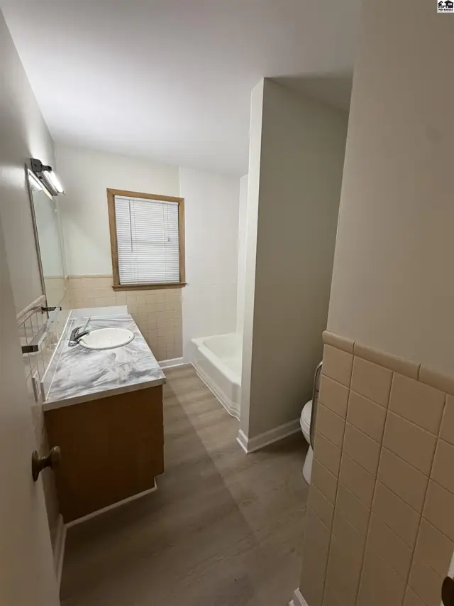 This bathroom features a vanity with a marble countertop, a bathtub, and tiled walls.