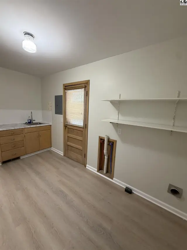 This room features a sink, wooden cabinets, shelving, and laundry hookups.