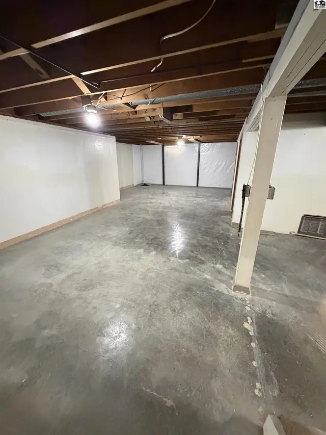 Unfinished basement with concrete floor, white walls, and exposed wooden ceiling beams.