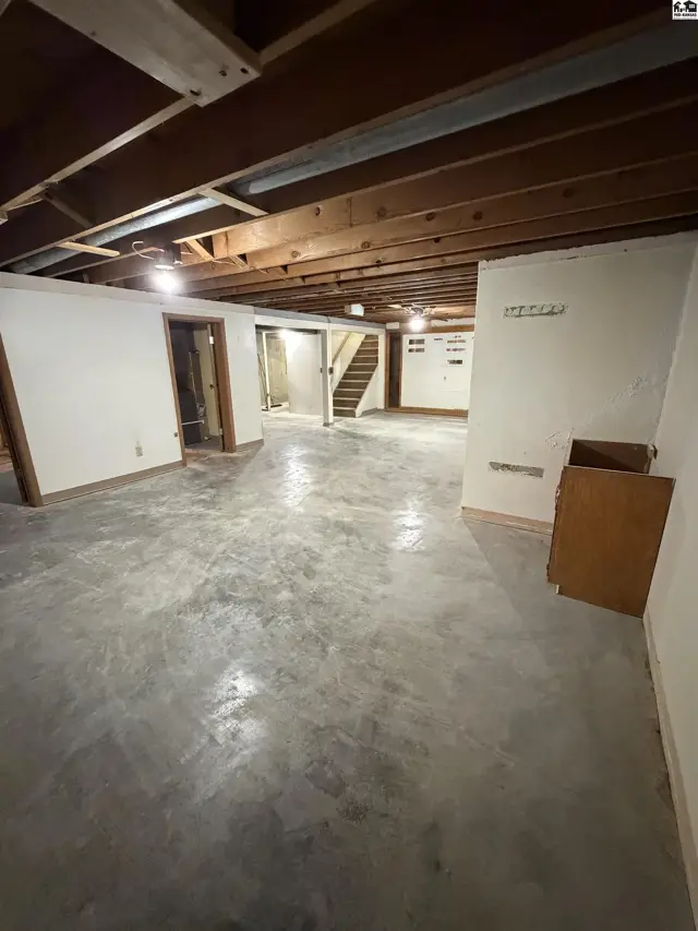 Unfinished basement with concrete floors, exposed wood joists, and a staircase.