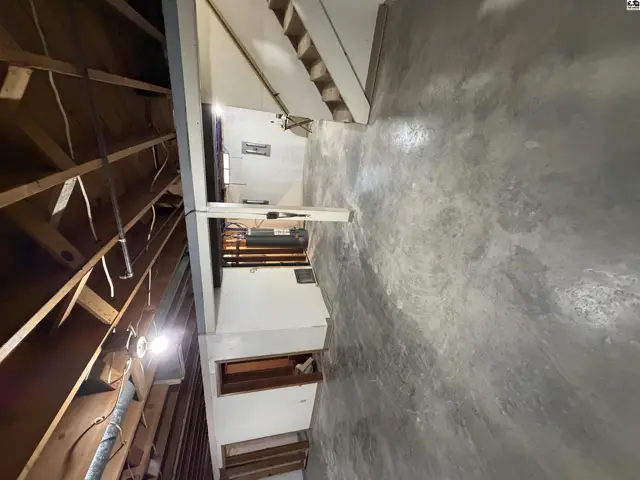 Concrete floor and unfinished wood ceiling in a basement area with stairs.