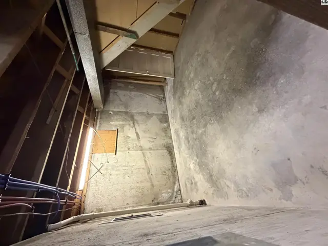 Attic space with exposed wooden beams and concrete walls.