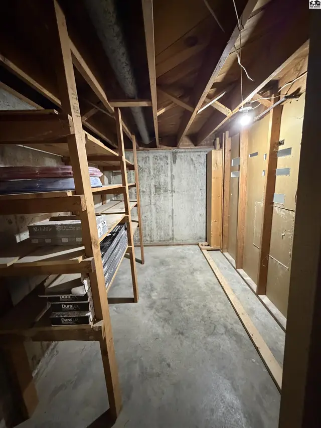 Unfinished basement with concrete floor, exposed joists, and wooden shelving.