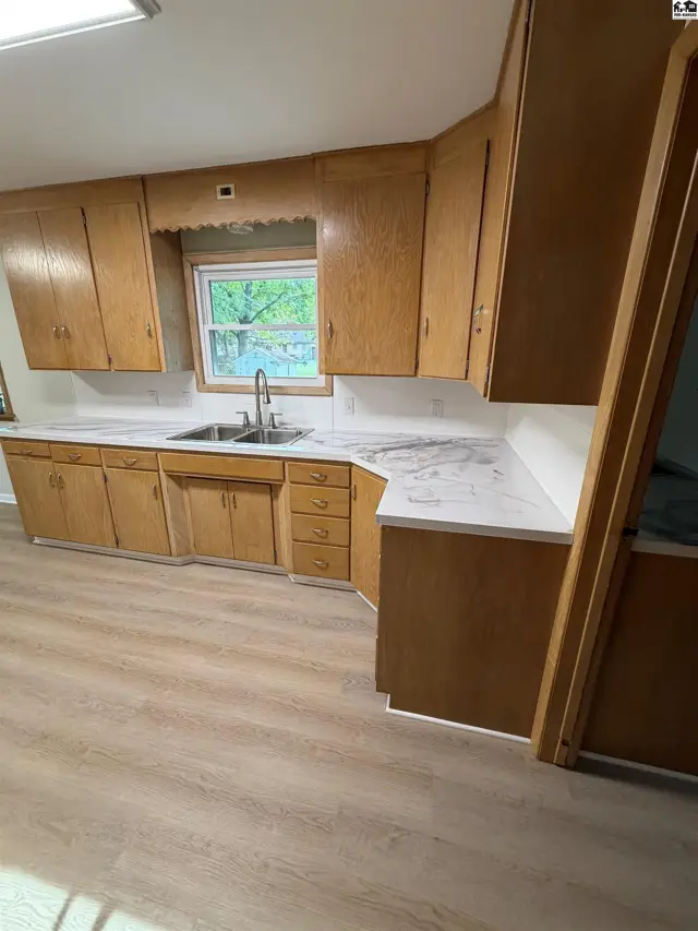 Kitchen features light wood cabinetry, white countertops, and a double sink.