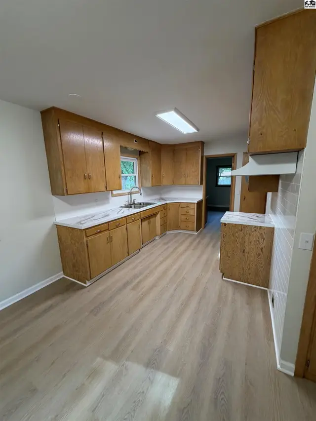 This kitchen features light wood cabinetry, white countertops, and a light wood-look floor.
