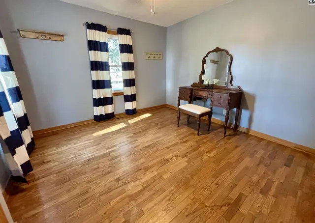 This room features hardwood floors, light blue walls, and a large window with striped curtains.