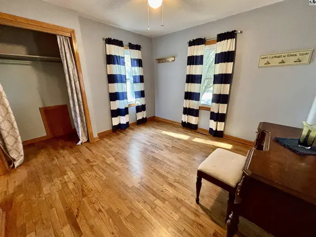 This room features hardwood floors, a closet, and two windows with striped curtains.