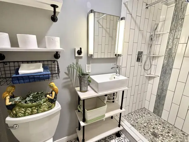 Modern bathroom features a pedestal sink, tiled shower, and decorative flooring.