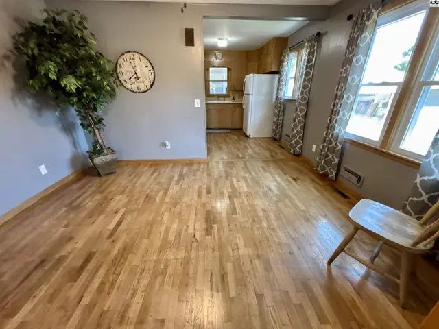 This living area features hardwood floors, a large wall clock, and a view into the kitchen.