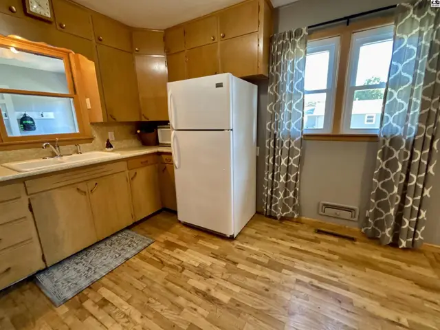 This kitchen features light wood cabinetry, a white refrigerator, and hardwood floors.