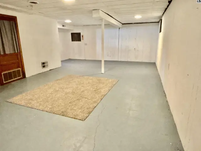 Spacious unfinished basement with concrete floor, white walls, and a large area rug.