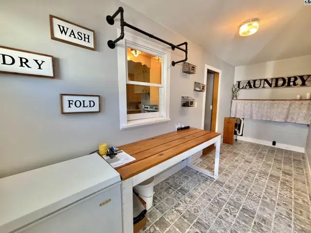 This laundry room features a long wooden countertop, tiled flooring, and wall-mounted shelving.