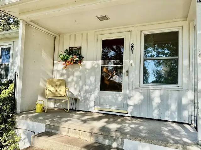 Covered porch with white siding, a yellow chair, and a window beside the front door.