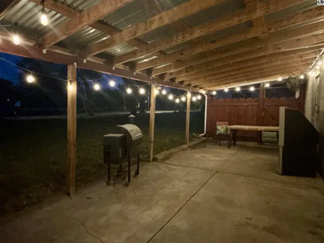 Covered patio with concrete floor, wooden posts, corrugated metal roof, and string lights.